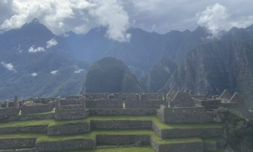 Das Bild zeigt eine Aufnahme von Terrassen in Machu Picchu. Dahinter ist eine Berglandschaft zu sehen.