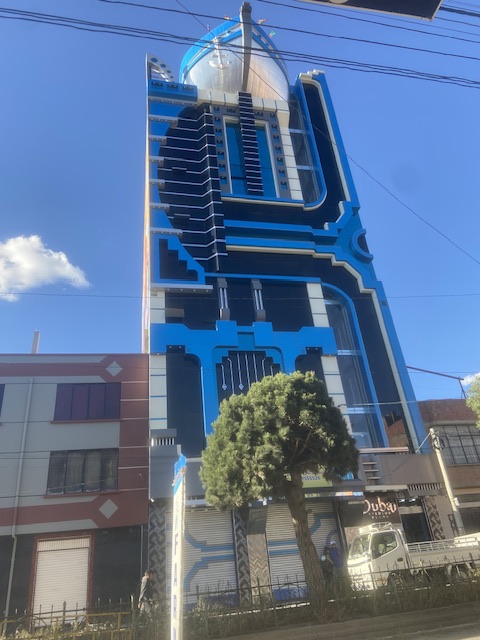 Das Bild zeigt die Fassade eines Cholet in El Alto. Die Fassade ist in blau gehalten - auf dem Dach ist ein großes Schiff zu sehen, wo sich auch ein Restaurant und eine Aussichtsplattform befindet.