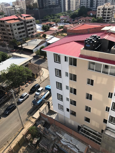 Das Bild zeigt ein Gebäude in Cochabamba, Bolivien. Aus diesem heraus wird ein Tankwagen mittels eines eigens dafür installiertem Rohr mit Leitungswasser betankt. Dafür steht der Tankwagen an der Straße. Das Wasser wird anschließend in Gegenden zu stark erhöhten Preisen verkauft, die ohne Leitungswasser versorgt werden.