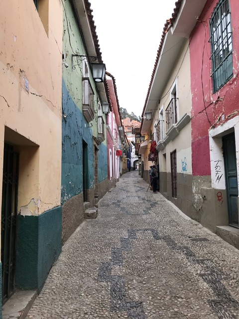 Das Bild zeigt eine Seitenstraße in La Paz. Zu sehen sind bunte Fassaden und indigene geometrische Motive auf dem Boden