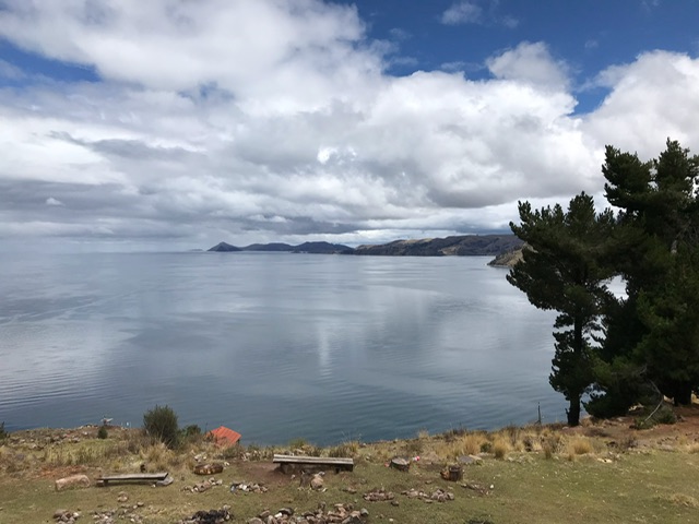 Das Bild zeigt einen Teil des Titicaca-Sees. Zu sehen ist das Wasser, Ufer und ein bewölkter Himmel.