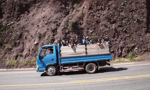 Das Bild zeigt einen Transportwagen, auf dessen Ladefläche Menschen kostengünstig mitfahren.