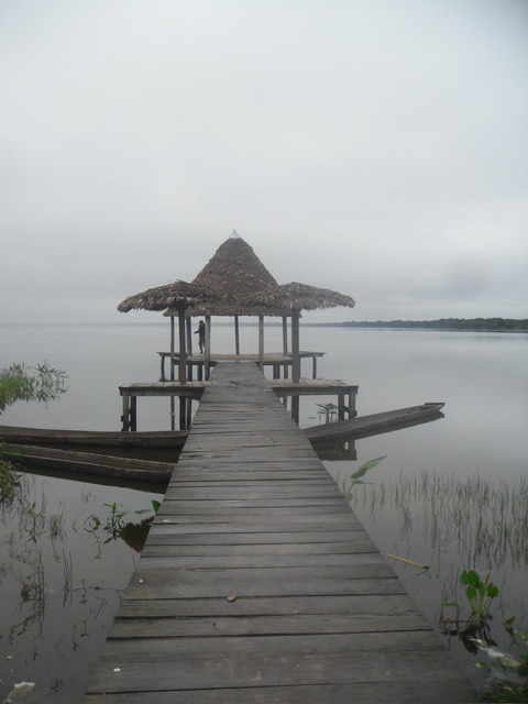 Das Bild zeigt eine tropische Landschaft in Beni, Bolivien. Zu sehen ist ein Steg mit einem Pavillion auf einem See.