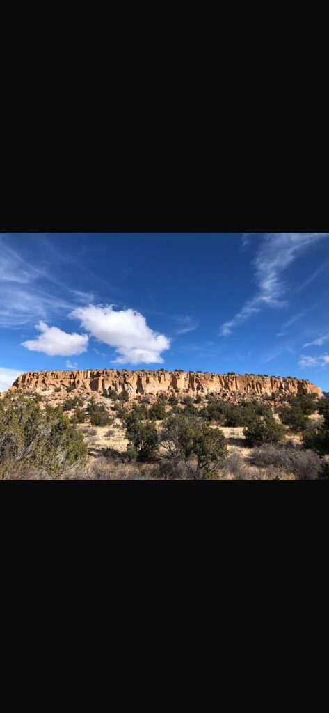 Das Bild zeigt die Ruinenstätte Tsankawi im Bandelier Nationalpark. Zu sehen ist eine Landschaft des nördlichen New Mexico. Tsankawi ist eine auf einem kleinen Plateau gelegene Ruinenstätte im Bandelier Nationalpark im nördlichen New Mexico. Neben den Überresten von Gebäuden, gibt es zudem in die Seitenwände des Kalksteinplateaus gehauene Behausungen.