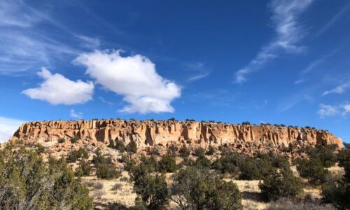 Das Bild zeigt die Ruinenstätte Tsankawi im Bandelier Nationalpark. Zu sehen ist eine Landschaft des nördlichen New Mexico. Tsankawi ist eine auf einem kleinen Plateau gelegene Ruinenstätte im Bandelier Nationalpark im nördlichen New Mexico. Neben den Überresten von Gebäuden, gibt es zudem in die Seitenwände des Kalksteinplateaus gehauene Behausungen.